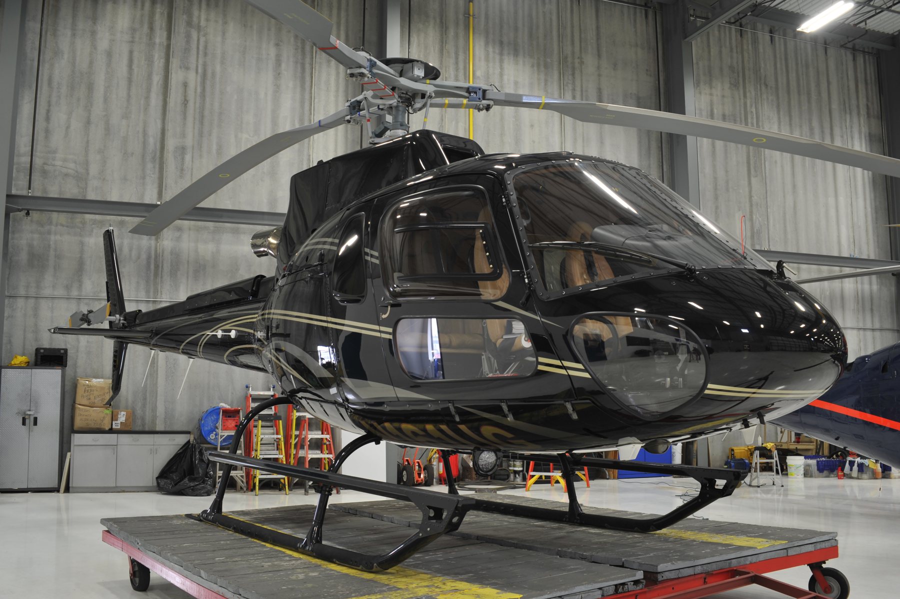 A gloss black helicopter with tan leather interior parked in a hangar