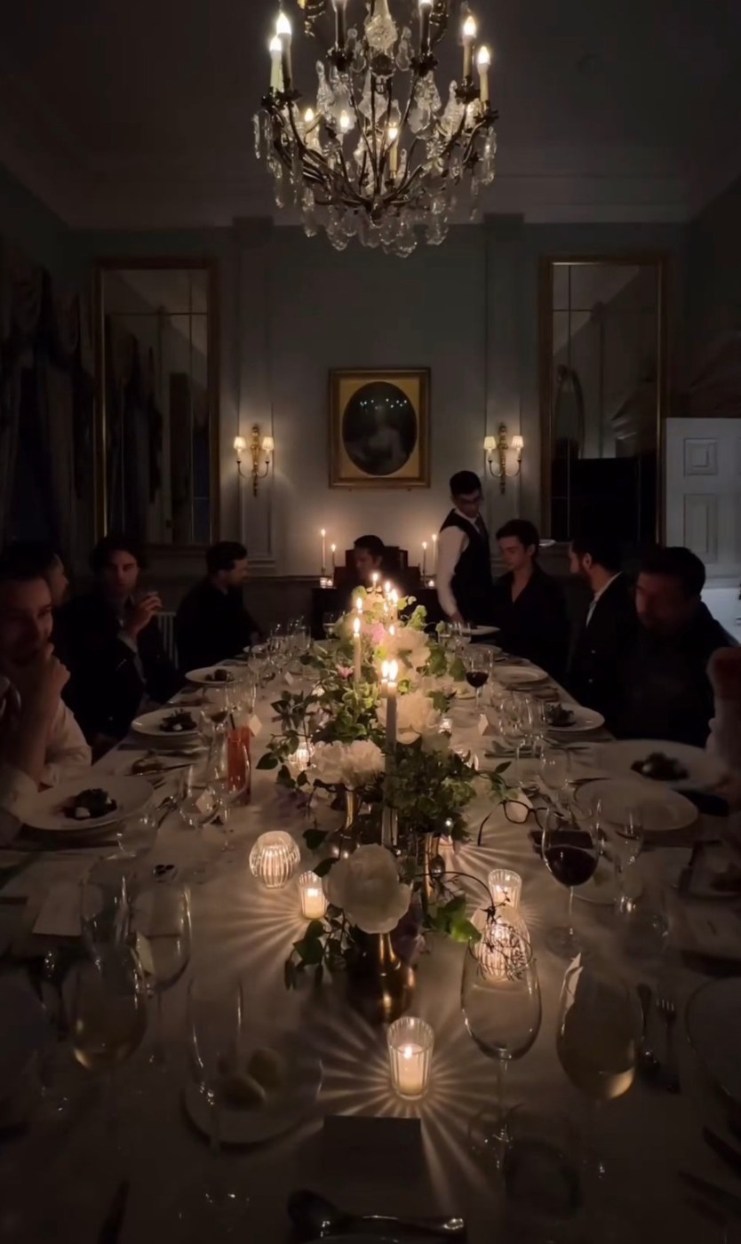 Guests at a long candlelit dinner table under a chandelier