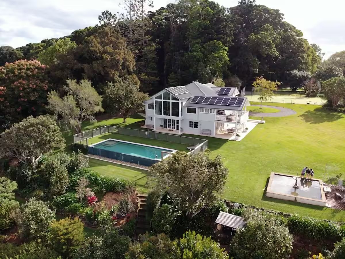 Aerial view of a white estate house with pool, lawn and tennis court surrounded by rainforest