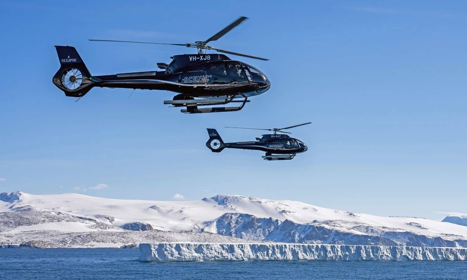 Two black helicopters flying over icebergs and snowy mountains